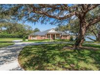 Stunning brick home featuring a circular driveway, manicured lawn, mature trees, and beautiful water view at 631 Old Mount Dora Rd, Eustis, FL 32726