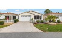 Charming single-story home featuring a white picket fence, well-manicured lawn, and attached garage at 2277 Whisper St, The Villages, FL 32162