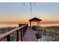 Scenic sunset view from the private boat dock on the water with boat lift, bench, and covered area at 11243 Dead River Rd, Tavares, FL 32778