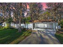 Charming single-story home featuring a screened-in porch and convenient carport with lush landscaping and mature trees at 11243 Dead River Rd, Tavares, FL 32778