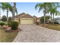 Charming single-Gathering home with stone accents, a paver driveway, lush landscaping, and mature palm trees at 1312 Patrick Pl, The Villages, FL 32162
