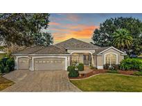 Charming single-story home featuring a manicured lawn, a three-car garage, and a brick paved driveway at 1339 Florence Path, The Villages, FL 32162