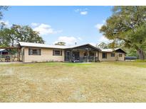 Tan home featuring a metal roof, a porch with black trim, and a large front yard with mature trees at 14100 Ne 46Th St, Silver Springs, FL 34488