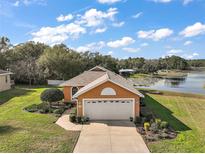 Charming single-Gathering home featuring a well-manicured lawn, attached garage, and a serene lake view at 125 Twin Lake Cir, Umatilla, FL 32784