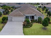 Well-maintained single-story home featuring an attached three-car garage, manicured lawn, and mature landscaping at 2935 Cedar Grove Loop, The Villages, FL 32163