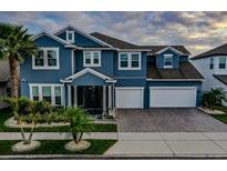 Charming two-story blue home featuring a two-car garage, lush landscaping and a brick driveway at 481 Blue Cypress Dr, Groveland, FL 34736