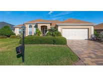 Charming single-story home featuring a well-manicured lawn, a two-car garage and tropical landscaping at 12239 Se 92Nd Court Rd, Summerfield, FL 34491