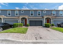 Exterior view of blue townhomes featuring a paver driveway, garages, manicured landscaping and red front doors at 384 Coral Beach Cir, Casselberry, FL 32707