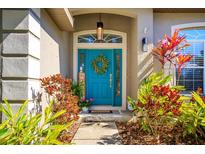 Inviting front entrance with a bright teal door, decorative wreath, transom window and colorful landscaping at 519 Hearthglen Blvd, Winter Garden, FL 34787