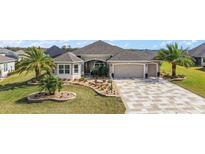 Well-manicured home exterior featuring a two-car garage, lush landscaping, and a paver driveway at 712 Krietemeyer Path, The Villages, FL 32163