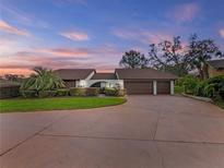 A spacious home featuring a three-car garage, mature landscaping, and a large, paved driveway at 9829 Wedgewood Ln, Leesburg, FL 34788