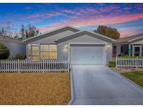 Charming home with white picket fence, attached garage, and well-manicured lawn at sunset at 1671 Campos Dr, The Villages, FL 32162