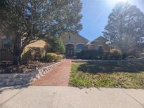 Inviting front exterior of a tan two-story home with mature trees and a brick walkway at 42316 E Saffron Ct, Eustis, FL 32736