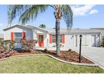 Charming single-story home featuring a well-manicured lawn, front-facing garage and a welcoming red front door at 9511 Se 168Th Elderberry Pl, The Villages, FL 32162