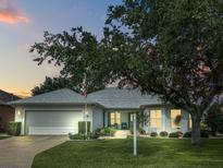 Charming single-story home with a well-manicured lawn, mature tree, and a two-car garage at dusk at 26821 Augusta Springs Cir, Leesburg, FL 34748