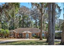 Charming brick home featuring mature trees and a well-manicured front lawn and circular driveway at 11215 Dead River Rd, Tavares, FL 32778