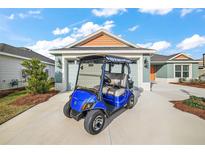 Charming single-Gathering home featuring a blue golf cart parked on a concrete driveway leading to an attached two-car garage at 2055 Merideth Ter, The Villages, FL 34762