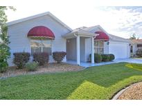 Charming single-story home featuring manicured lawn, well-maintained landscaping, and red awnings over the windows at 1229 Augustine Dr, The Villages, FL 32159