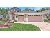 Beige two story home featuring a two car garage, front lawn, and landscaping at 20751 Queen Alexandra Dr, Leesburg, FL 34748