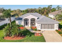 Beautiful single-story home featuring a gray roof, a three-car garage, and lush landscaping with vibrant plants and palm trees at 27023 Old English Ct, Leesburg, FL 34748