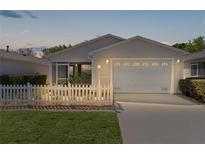 Charming home featuring a well-kept lawn, picket fence, and attached two-car garage at 2594 Ascot Loop, The Villages, FL 32162