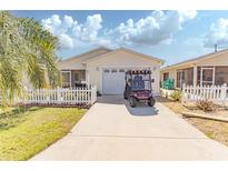 Charming single-story home featuring a well-manicured lawn, white picket fence, and a convenient golf cart parked on the driveway at 992 Ridgeville Rd, The Villages, FL 32162