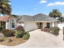 Charming single-story home with a well-manicured lawn, palm trees and a driveway leading to the garage at 557 Harlow Ln, The Villages, FL 32163