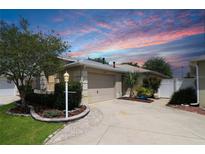 Charming home featuring a beige exterior, lush landscaping, and an attached two-car garage at 1135 Easley Way, The Villages, FL 32162