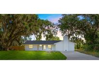 Charming single-story home with a white brick exterior, green lawn, and mature trees draped in Spanish moss at 2517 Royal Palm Dr, Edgewater, FL 32141