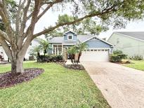 Charming blue home featuring a two-car garage, beautiful landscaping, and a well-manicured lawn at 3275 Oak Brook Ln, Eustis, FL 32736