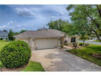 Inviting single-story home featuring a well-manicured lawn, mature landscaping, and a spacious two-car garage at 725 Beldon Ct, The Villages, FL 32162