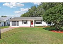 Charming single-story home with a well-manicured lawn, red door, and mature trees at 915 Sutherland Ct, Leesburg, FL 34788
