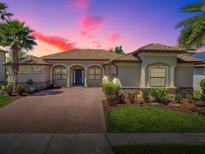 Charming home showcasing a paver driveway, manicured lawn, and lush landscaping with palms against a vibrant twilight sky at 1408 Deuce Cir, Davenport, FL 33896