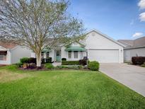 Charming white home with well-manicured lawn, mature tree, green awnings and attached garage at 2103 Patino Ln, The Villages, FL 32159