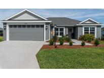 Charming single-story home featuring a well-manicured lawn and a gray two-car garage at 1422 Jeremy Cir, The Villages, FL 34762
