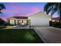 Charming single-story home with a well-manicured lawn, inviting patio, and two-car garage, set against a colorful sunset sky at 2290 Due West Dr, The Villages, FL 32162