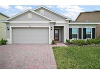 Charming single-Gathering home featuring a two-car garage, red brick driveway, and well-manicured landscaping at 444 Shadow Gorge Way, Eustis, FL 32736