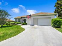 Well-maintained home showcasing a curved driveway, manicured lawn and white exterior with an American flag at 11702 Se 173Rd Lane Rd, Summerfield, FL 34491