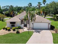 Charming home with a well-manicured lawn, lush landscaping, and a concrete driveway leading to an attached garage at 2461 Merida Cir, The Villages, FL 32162