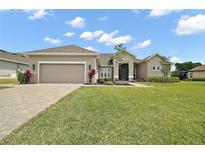 Charming single Gathering home featuring a well-manicured lawn, paver driveway, and two-car garage at 5195 Greens Dr, Lady Lake, FL 32159