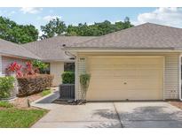 Beige two car garage with neutral siding and walkway to the front door surrounded by lush landscaping at 340 Juniper Way, Tavares, FL 32778