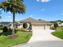 Beautiful single-story home with a three-car garage, lush landscaping, and a palm tree at 973 Baisley Trl, The Villages, FL 32162