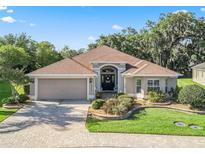 Charming single-story home features a well-manicured lawn, brick driveway, and a welcoming front entrance with garden beds at 10069 Lake Miona Way, Oxford, FL 34484