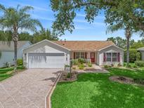 Charming single-story home with a well-manicured lawn, lush landscaping, and brick paver driveway at 2259 Lockwood Loop, The Villages, FL 32162