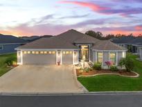 Stunning single-story home featuring a three-car garage, manicured lawn, and beautiful landscaping at dusk at 4406 Creighton Loop, The Villages, FL 32163
