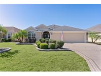 Charming single-story home featuring a manicured lawn, landscaped garden beds, and a welcoming two-car garage at 1754 Pennecamp Dr, The Villages, FL 32162