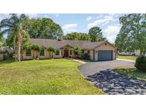 Inviting single-story home with lush landscaping, a spacious front yard, and an attached two-car garage at 12504 Blue Heron Way, Leesburg, FL 34788