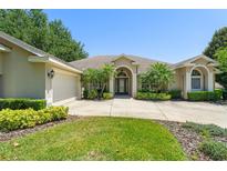 Inviting single-story home featuring a well-manicured lawn, arched entryway, and mature landscaping at 13045 Colonnade Cir, Clermont, FL 34711