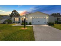 Charming home featuring a well-manicured lawn, light-colored siding, and an attached two-car garage at 17385 Se 76Th Champion Ave, The Villages, FL 32162