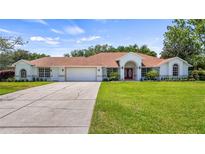 Beautiful single-story home featuring a well-manicured lawn, red double door entrance, and attached two car garage at 17825 Whisperwind Dr, Clermont, FL 34715